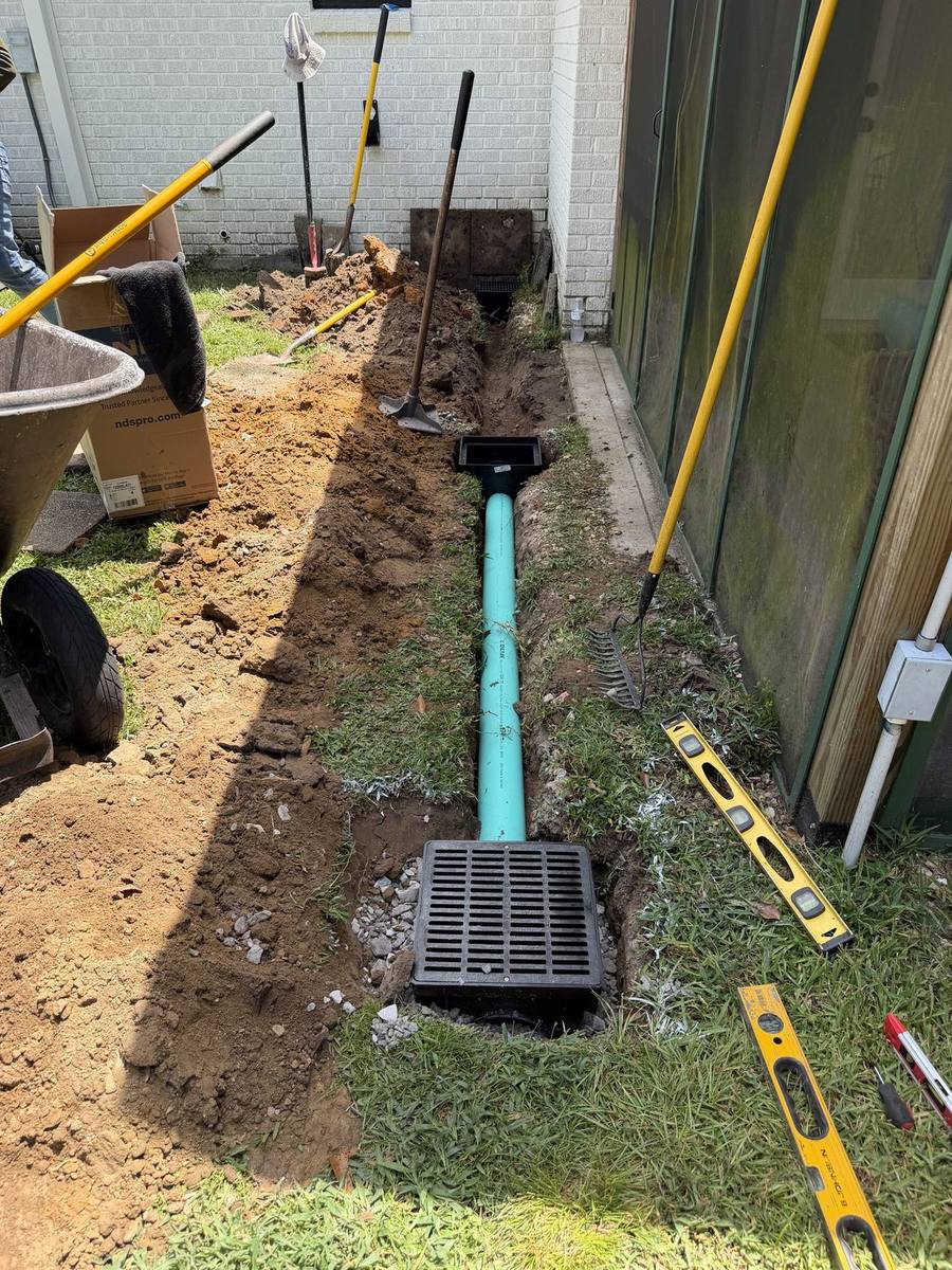 Catch basin grate set level in a freshly dug drainage trench beside a home