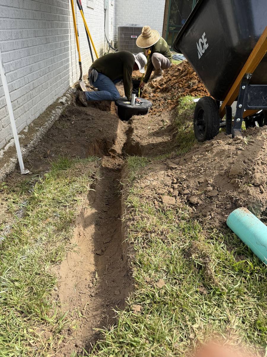 SOTE crew member running a mini excavator to dig a drainage trench across a Northshore lawn